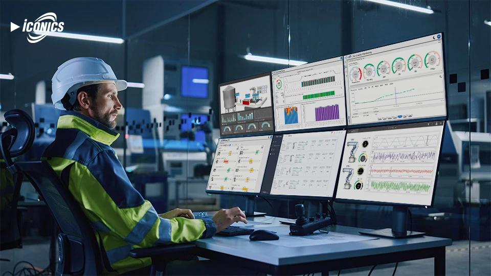 Photo of man wearing a hard hat and high-visibility jacket sitting at a desk with six monitors featuring different dashboard views